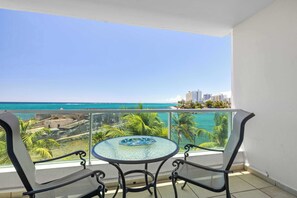 Ein Balkon mit Glastisch und zwei Stühlen, mit Blick auf Strand und Meer.