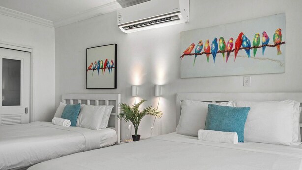 Habitación de hotel con dos camas, una planta en maceta, decoración en la pared y aire acondicionado en el techo.