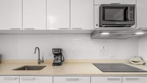 Una cocina con armarios blancos, microondas integrado, cafetera y lavamanos.
