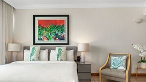 Ett hotellrum med en säng, två sänglampor, ett nattduksbord, en stol, en inramad tavla och en krukväxt.