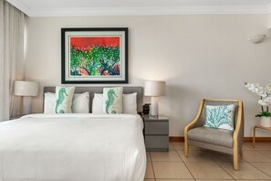 Ein Hotelzimmer mit einem Bett, zwei Nachttischlampen, einem Nachttisch, einem Sessel, einem gerahmten Gemälde und einer Topfpflanze.