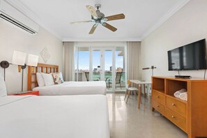 A hotel room with two beds, a ceiling fan, a TV, a desk, and a view of the city. - Lagoon Front 3BR - Balconies & Pool (San Juan)