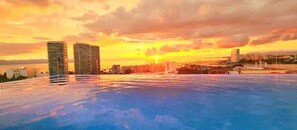 Eine Stadtsilhouette bei Sonnenuntergang über einem Gewässer, mit hohen Wolkenkratzern und blauem Himmel.