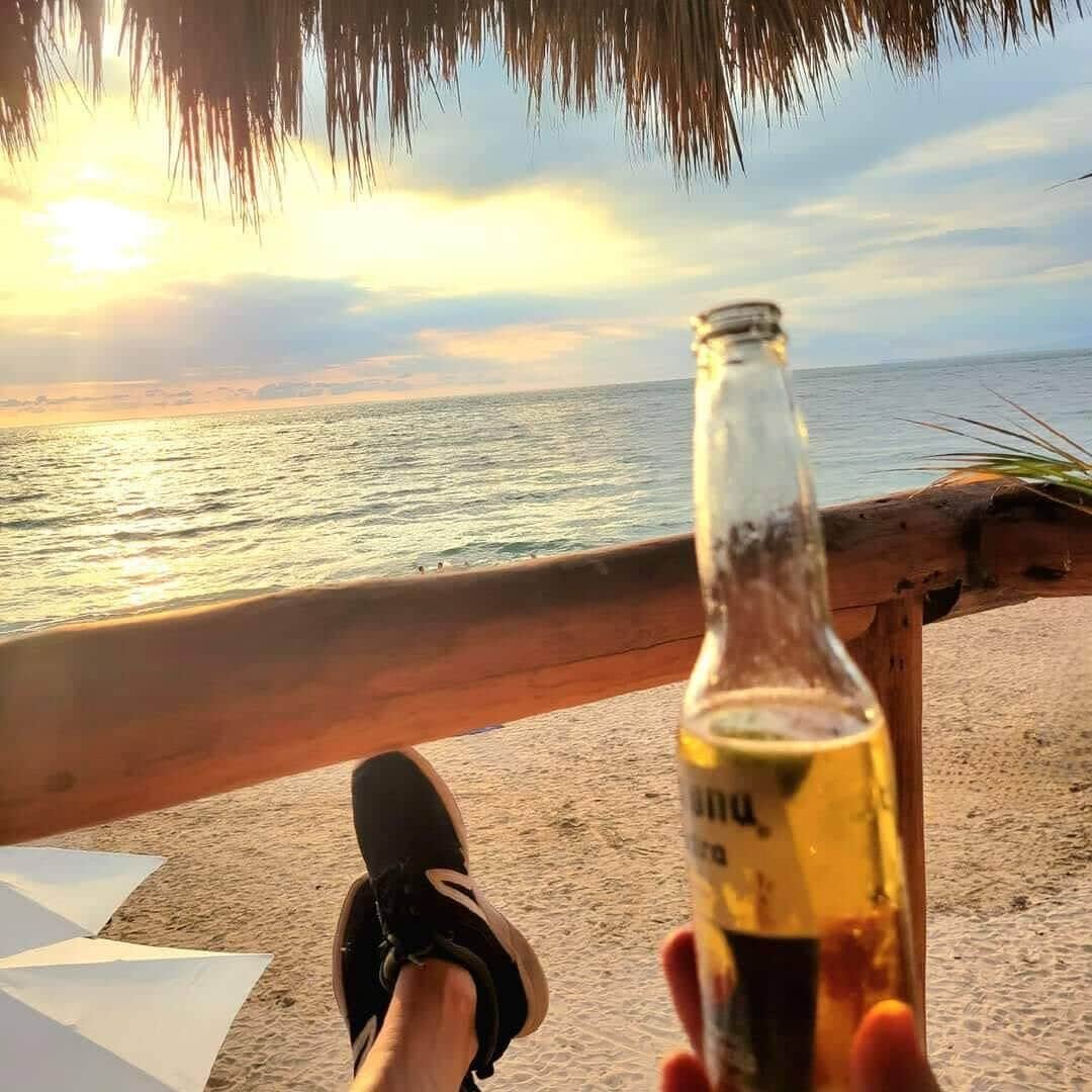 Blick auf einen Strand mit einem Holgitter und einem Getränk in der Hand.