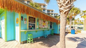 Un bar tiki con fachada azul, techo de paja y taburetes verdes.