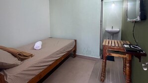 A small, single-bed room with a wooden bed, a small table, a wall-mounted TV, and a sink.