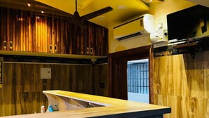 A hotel room with a wooden panel wall, a ceiling fan, an air conditioning unit, and a television mounted on the wall.