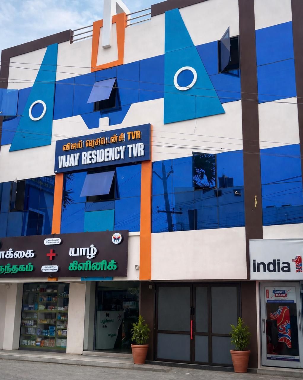 A building with a sign for 'VIJAY RESIDENCY TVR' and a pharmacy with Tamil signage.