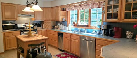 A kitchen with wooden cabinets, a stainless steel dishwasher, a coffee maker, and a window with a view of greenery.