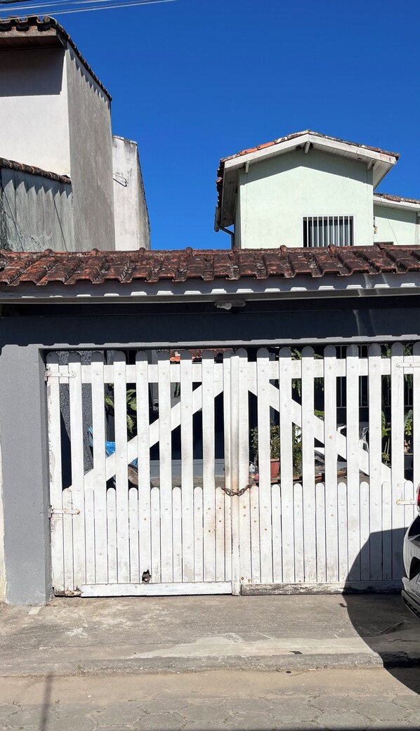 Une entrée fermée par un portail en métal et une allée en béton menant à un bâtiment doté d’un toit recouvert de tuiles.