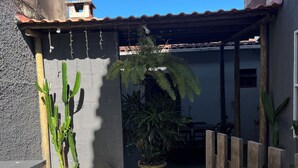 Un camí estret que condueix a una zona exterior coberta, amb una tanca de fusta, plantes en testos i un edifici amb teulada de rajola.