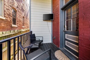 A small outdoor seating area with a table and chairs, a TV mounted on the wall, and a door with a window. - The Benton Lounge "Historic Home Near Downtown" (St. Louis)