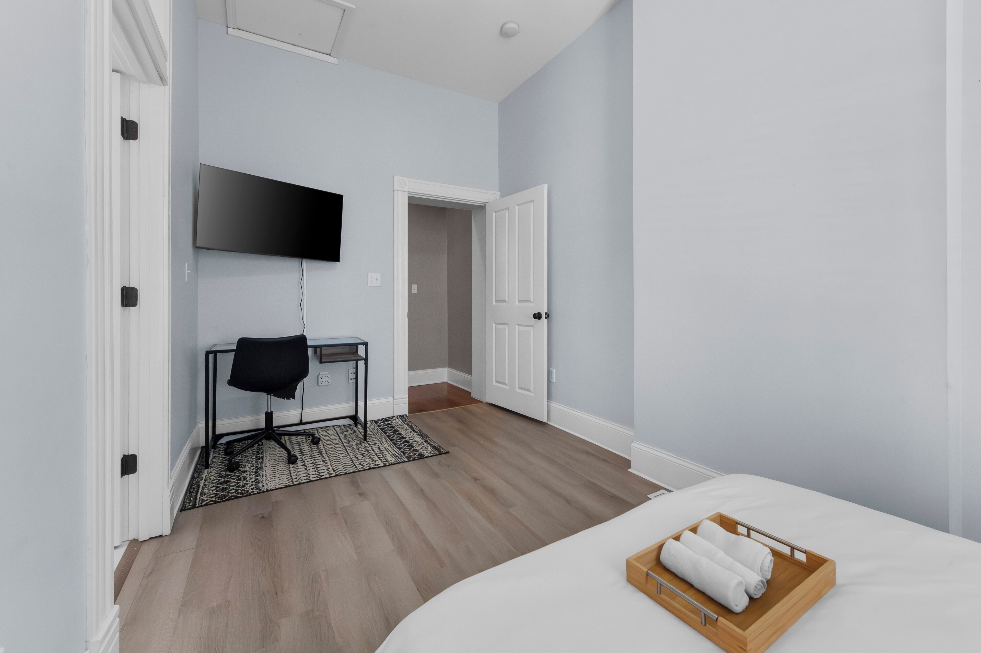 Une chambre d’hôtel comprenant un lit, un téléviseur fixé au mur, un bureau avec une chaise et un plateau en bois avec des serviettes.