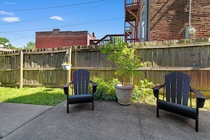 A patio area with two Adirondack chairs and a large planter with a small tree. - The Benton Lounge "Historic Home Near Downtown" (St. Louis)