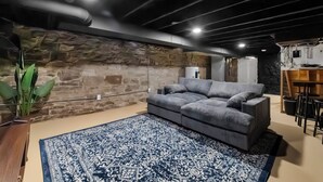 Uma sala de estar moderna com uma parede de pedra, um sofá cinza e um tapete estampado.