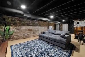 A modern living room with a stone wall, a grey sofa, and a patterned rug. - The Benton Lounge "Historic Home Near Downtown" (St. Louis)