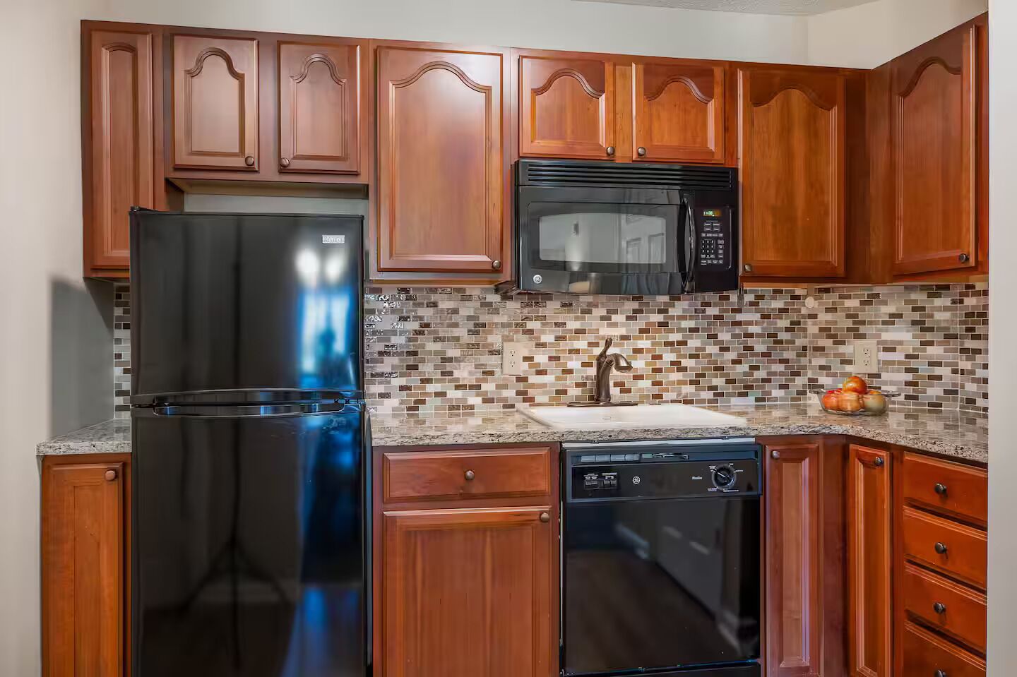 A kitchen with wooden cabinets, a stainless steel refrigerator, a microwave, a dishwasher, and a tiled backsplash.
