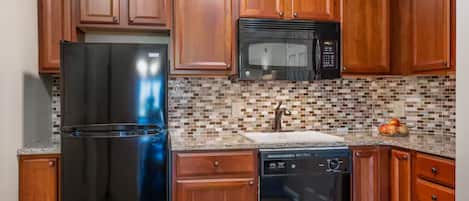 A kitchen with wooden cabinets, a stainless steel refrigerator, a microwave, a dishwasher, and a tiled backsplash.