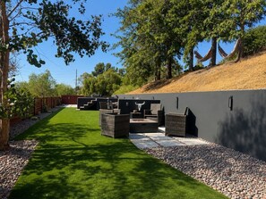 A modern outdoor seating area with wicker furniture and a stone wall backdrop. - Golden Hill Retreat with Private Hot Tub (Spring Valley)