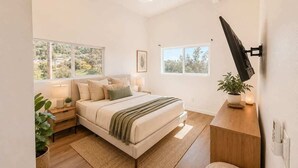 Une chambre moderne avec un grand lit, des tables de chevet, un bureau et un téléviseur fixé au mur.