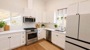 Une cuisine moderne avec des armoires blanches, des appareils en acier inoxydable et un plancher en bois.