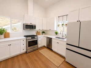 A modern kitchen with white cabinets, stainless steel appliances, and a wooden floor. - Golden Hill Retreat with Private Hot Tub (Spring Valley)