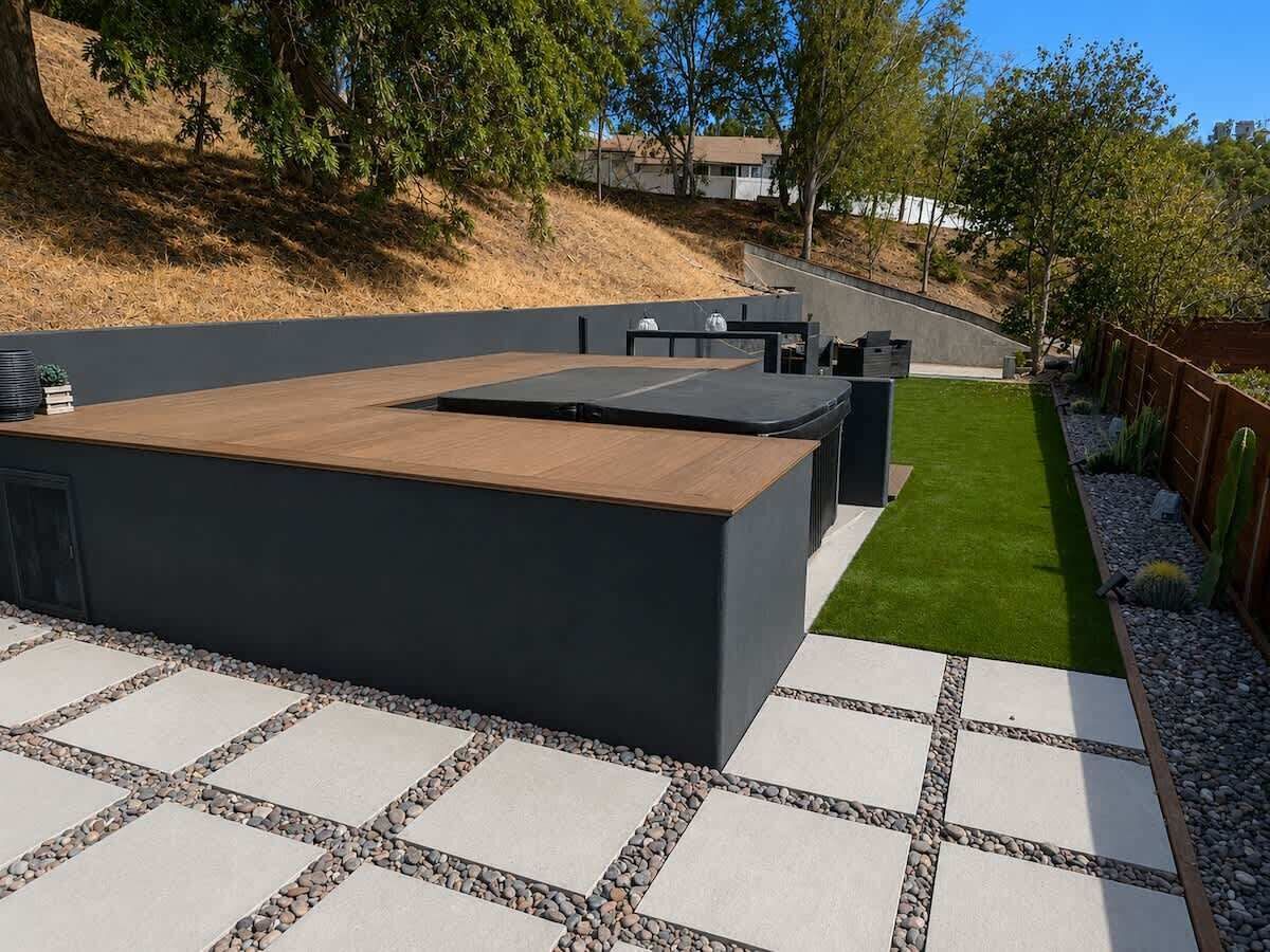 Une terrasse extérieure moderne dotée d’une surface plane, d’un espace salon et d’un chemin menant à une pelouse verdoyante.