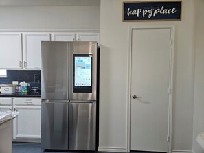 A stainless steel refrigerator with a digital interface, white cabinetry, and a door with a sign above it. - Cozy 3 Bedroom Home Near Frisco's Best Spots- Stylish&Comfy (Little Elm)