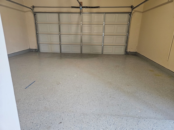 A garage with a closed garage door, concrete floor, and metal garage door opener.