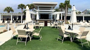 A poolside area with artificial grass, lounge chairs, and umbrellas. - BlueNote by Sandpiper | Near North Beach (Seabrook Island)