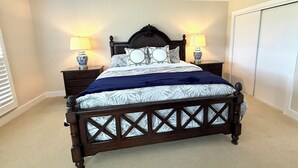 A bedroom with a dark wooden bed, two bedside tables with lamps, a large window with blinds, and a wardrobe. - BlueNote by Sandpiper | Near North Beach (Seabrook Island)