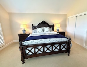 A bedroom with a dark wooden bed, two bedside tables with lamps, a large window with blinds, and a wardrobe. - BlueNote by Sandpiper | Near North Beach (Seabrook Island)