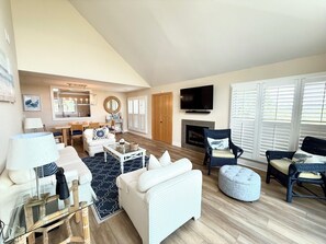 A spacious living room with a high ceiling, a fireplace, and a television mounted on the wall. - BlueNote by Sandpiper | Near North Beach (Seabrook Island)