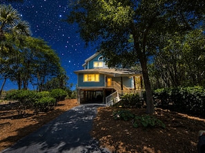 A two-story house with a covered porch, surrounded by trees and a starry night sky. - BlueNote by Sandpiper | Near North Beach (Seabrook Island)