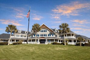 A large, multi-story building with a prominent American flag, multiple balconies, and a well-maintained lawn. - The Retreat by Sandpiper | Near Beach (Seabrook Island)