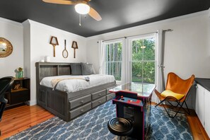 A bedroom with a bed, a desk with a chair, a ceiling fan, and a window with curtains. - The Retreat by Sandpiper | Near Beach (Seabrook Island)