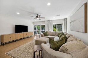 A modern living room with a flat-screen TV, a sofa set, a wooden cabinet, and a ceiling fan. - 1212 Lagoon Villas | Sleeps 4 (Fernandina Beach)