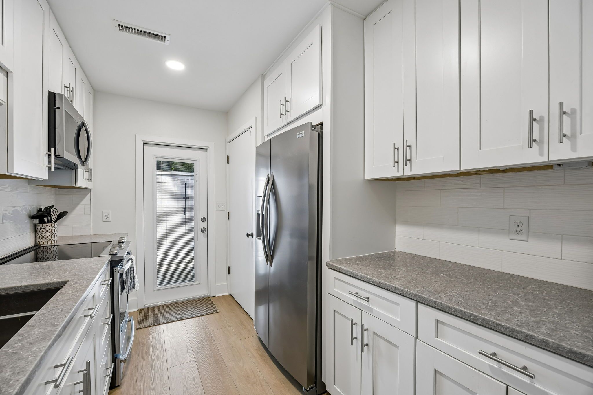 A modern kitchen with white cabinetry, stainless steel appliances, and a granite countertop.