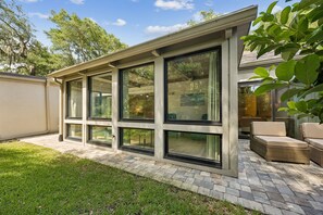 A modern patio with a glass enclosure, outdoor furniture, and a brick pathway. - 1212 Lagoon Villas | Sleeps 4 (Fernandina Beach)