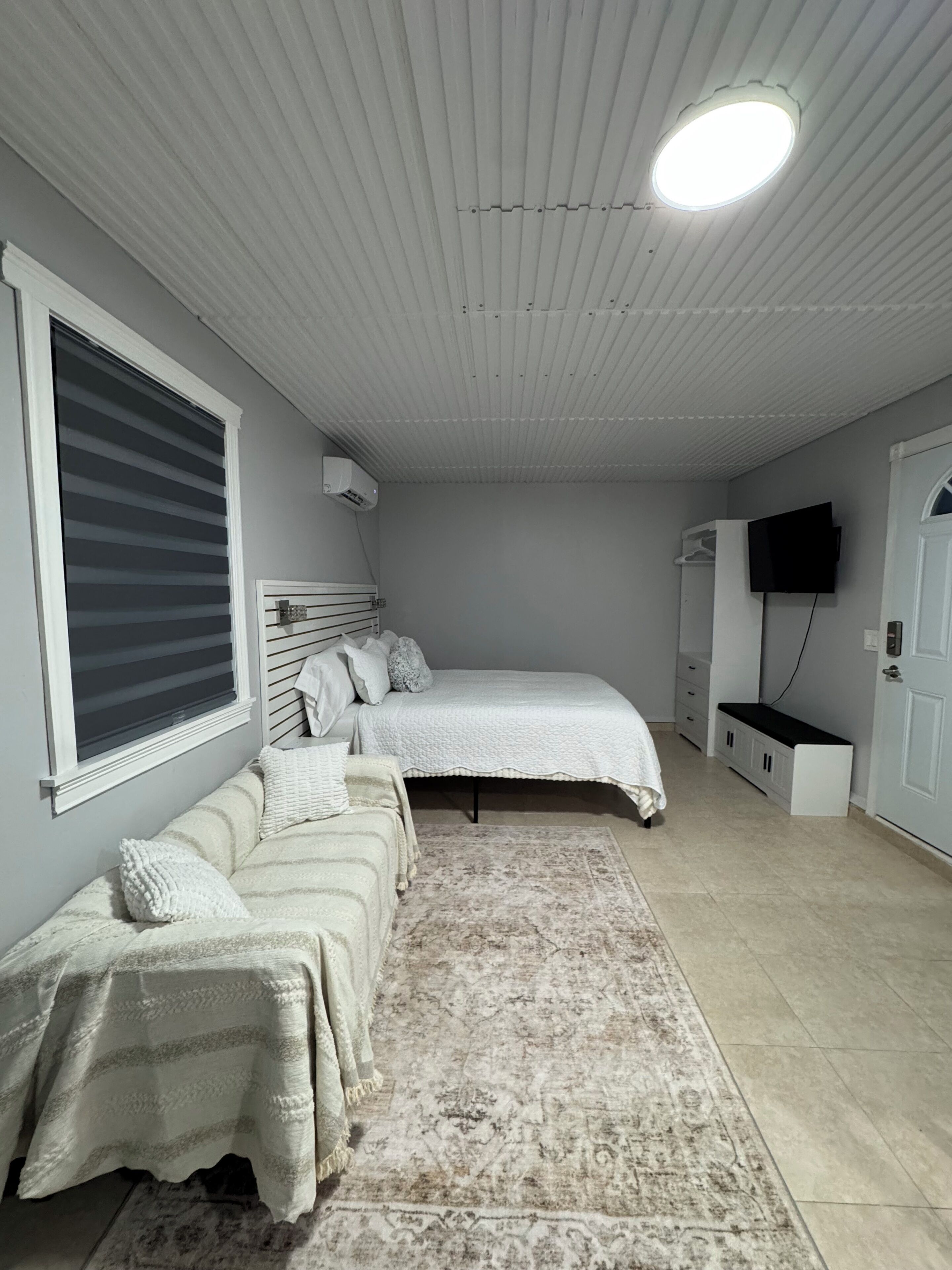 Une chambre à coucher avec un lit, un banc, une télévision et une fenêtre avec des stores.