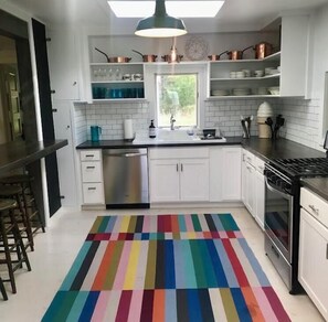 A kitchen with white cabinets, stainless steel appliances, and a colorful striped rug. - 5 Pines Farmhouse | Historic Madeline Island Retreat Near Lake Superior (La Pointe)