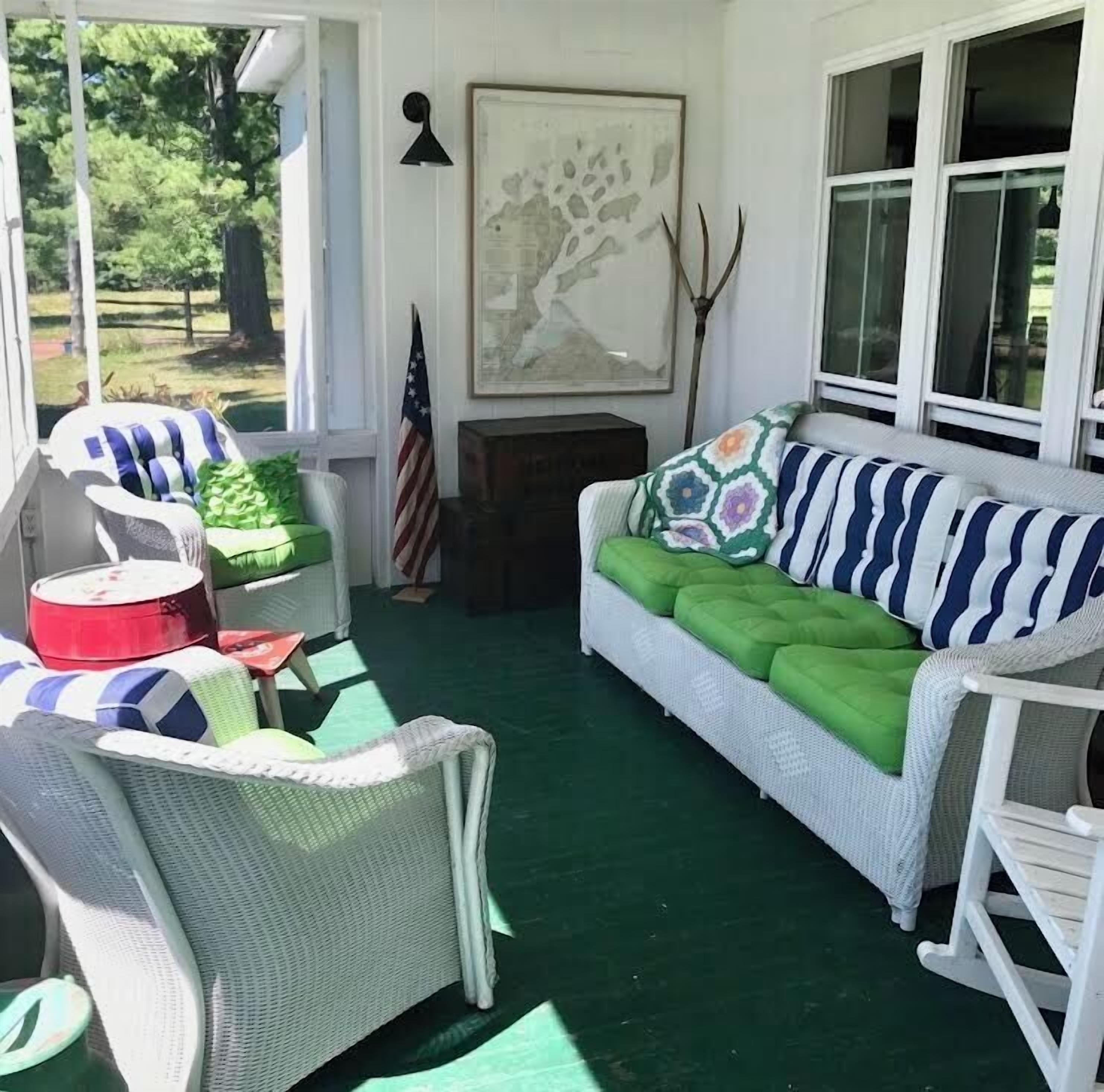 A covered porch with wicker furniture, a green cushioned sofa, and an American flag.