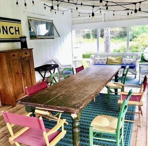A rustic dining area with a wooden table and colorful chairs, a bench with cushions, and a view of greenery outside. - 5 Pines Farmhouse | Historic Madeline Island Retreat Near Lake Superior (La Pointe)