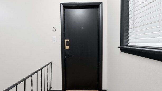 A black door with a keypad lock, a number '3' sign above it, and a window with blinds to the right.