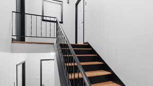 A staircase with wooden steps and black railings, leading to a landing with a door and a window.