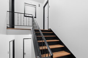 A staircase with wooden steps and black railings, leading to a landing with a door and a window.