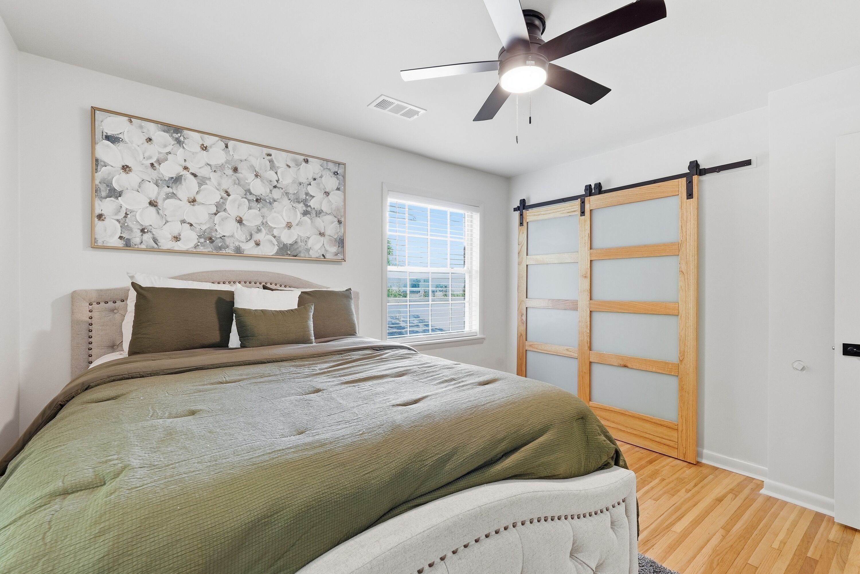 Une chambre à coucher avec un lit, un ventilateur de plafond, une fenêtre et une porte coulissante.