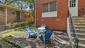 A brick building with a white door and a window, a set of outdoor stairs, and blue chairs and a table.