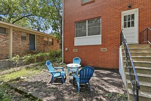 A brick building with a white door and a window, a set of outdoor stairs, and blue chairs and a table.