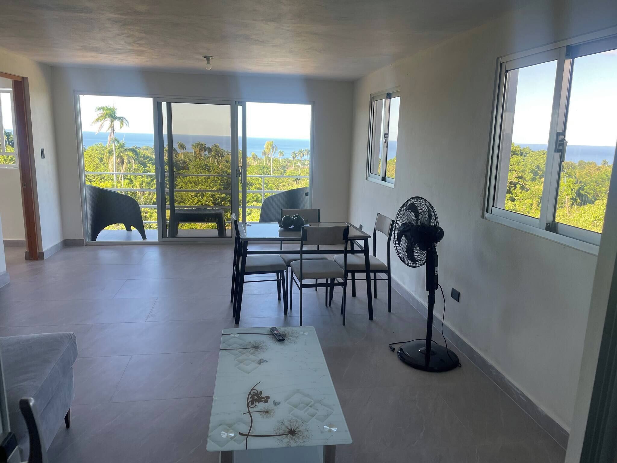 Een ruim balkon met een tafel en stoelen, een ventilator en uitzicht op de oceaan.